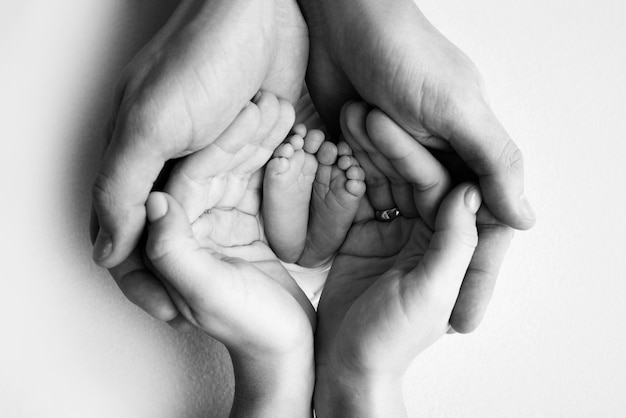 Photo the palms of the father, the mother are holding the foot of the newborn baby. feet of the newborn on the palms of the parents. photography of a child's toes, heels and feet. black and white photo.