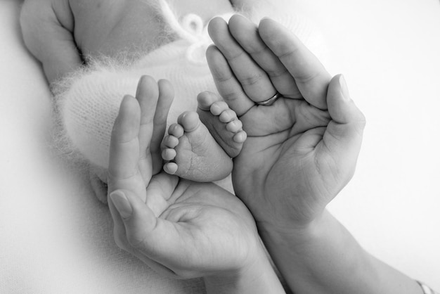 The palms of the father, the mother are holding the foot of the newborn baby. Feet of the newborn on the palms of the parents. Studio photography of a child's toes, heels and feet. Black and white.