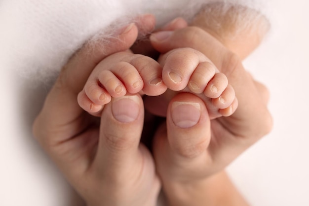 The palms of the father, the mother are holding the foot of the newborn baby. Feet of the newborn on the palms of the parents. Studio photography of a child's toes, heels and feet. Concept.