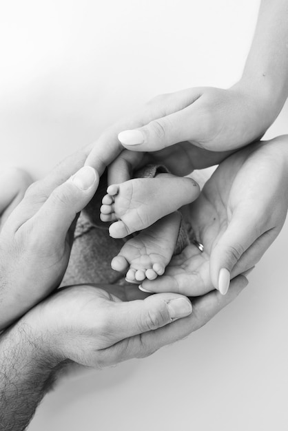 The palms of the father the mother are holding the foot of the newborn baby on white background Feet of the newborn on the palms of the parents Photography of a child's toes heels and feet