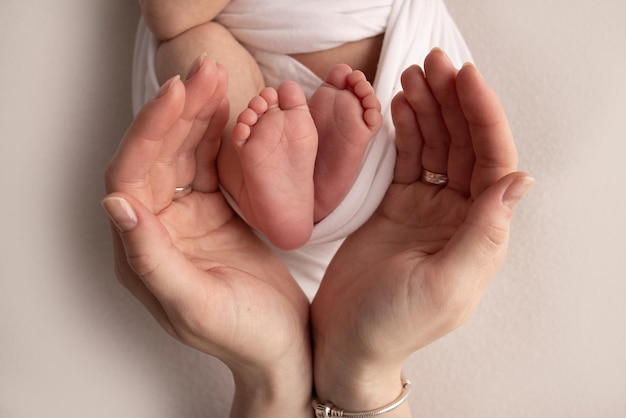 The palms of the mother are holding the foot of the newborn baby in a white blanket Feet of the newborn on the palms of the parents Studio macro photo of a child39s toes heels and feet