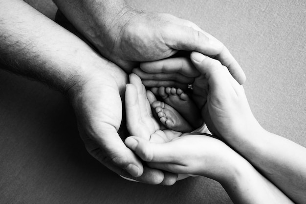 The palms of the parents A father and mother hold the feet of a newborn child The feet of a newborn in the hands of parents Photo of foot heels and toes Black and white