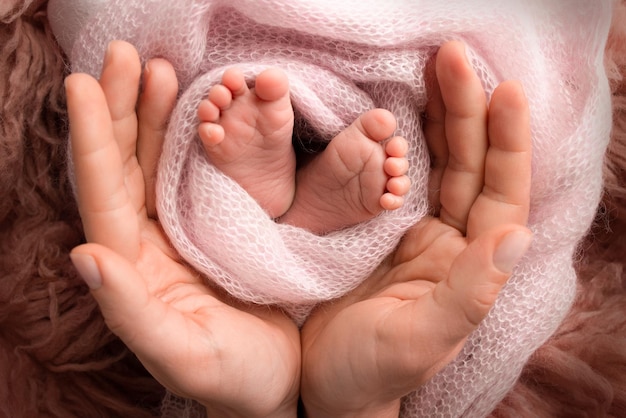 The palms of the parents A father and mother hold the feet of a newborn child in a pink blanket on a brown background The feet of a newborn in the hands of parents Photo of foot heels and toes