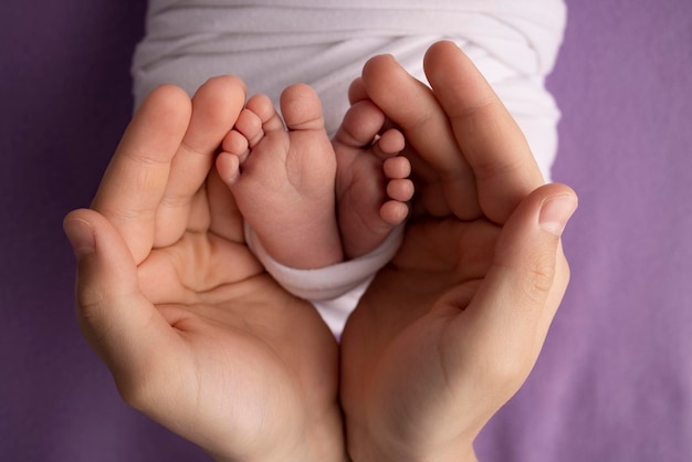 両親の手のひら父と母は、紫色の背景に白い毛布で生まれたばかりの子供の足を持っています両親の手で新生児の足足のかかととつま先の写真