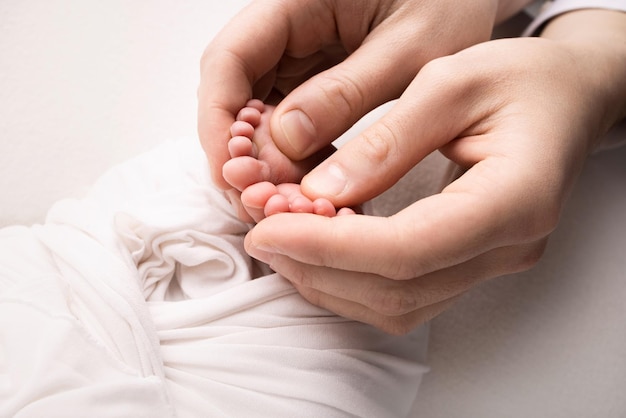 The palms of the parents A father and mother hold the feet of a newborn child in a white blanket on a white background The feet of a newborn in the hands of parents Photo of foot heels and toes