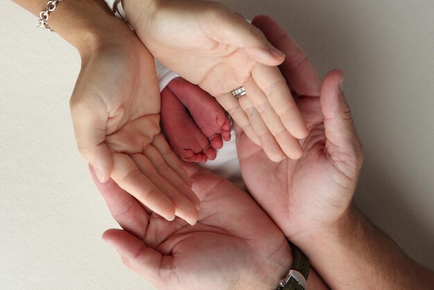 Пальмы родителей, отец и мать, держат ноги, ноги новорожденного ребенка в белой оболочке на белом фоне, ноги, каблуки и пальцы ног новорожденого ребенка вблизи.