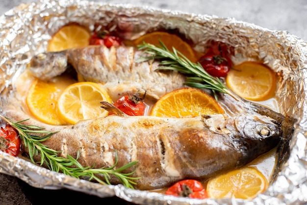 Foto una teglia di pesce al forno con sopra rosmarino e pomodorini.