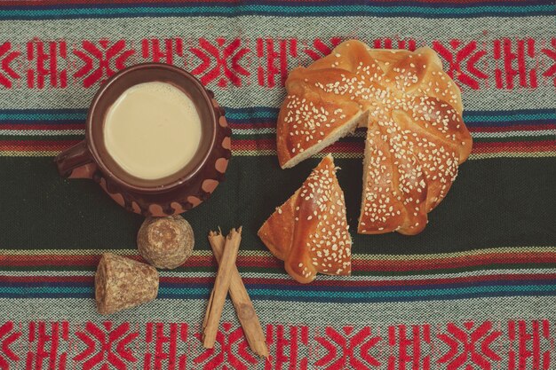 Pan de muerto y taza de 초콜릿 sobre una mesa con mantel tipico mexicano