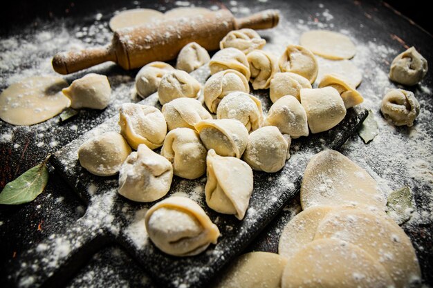 A pan of dumplings with flour on it and a rolling pin on the side.