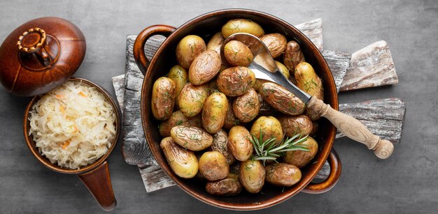 Pan filled with roasted potatoes shot on rustic wooden table. The ingredients includes are raw potatoes, rosemary, dill, salt, pepper and garlic.