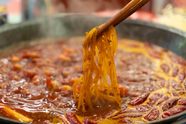 Una padella di cibo con un cucchiaio di legno e alcuni noodles in esso