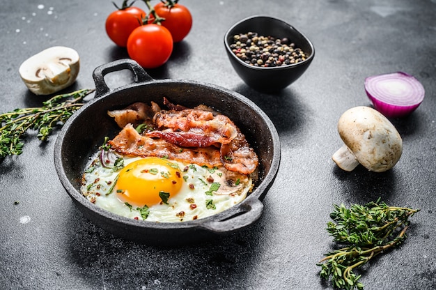 Pan of fried eggs with bacon and fresh tomato