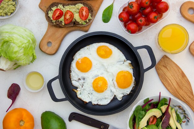 Pan of fried eggs with vegetarian sandwich with avocado