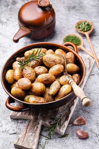 Pan gevuld met geroosterde aardappelen geschoten op rustieke houten tafel. De ingrediënten zijn onder meer rauwe aardappelen, rozemarijn, dille, zout, peper en knoflook.