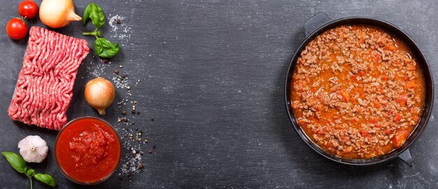 Pan met bolognese saus en ingrediënten om te koken, bovenaanzicht met kopie ruimte