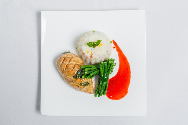 Pan roasted chicken breast with long green beans and light vegetable rice platter Food decorating with red sauce on a white plate Isolated white background