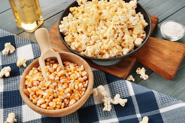 Pan vol traditionele popcorn en kom met maïskorrel op houten tafel