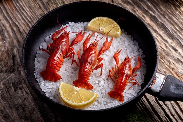 A pan with boiled crayfish stands on a textured brown wooden table top. View from above.