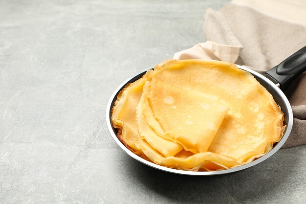 Pan with thin pancakes and kitchen towel on gray background