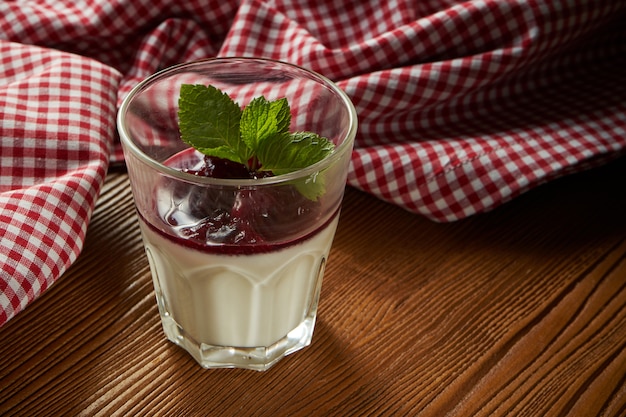 Panakota with red greasy berry in a glass on a wooden background.