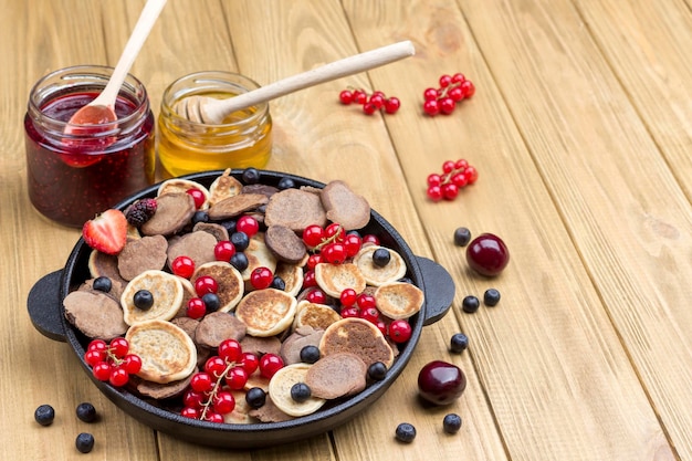 Pancake and berries in pan Honey and jam on table Light wood background Top view Copy space