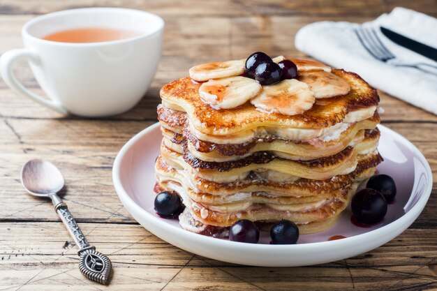 Pancake cake with bananas and berry syrup, selective focus, dark background.