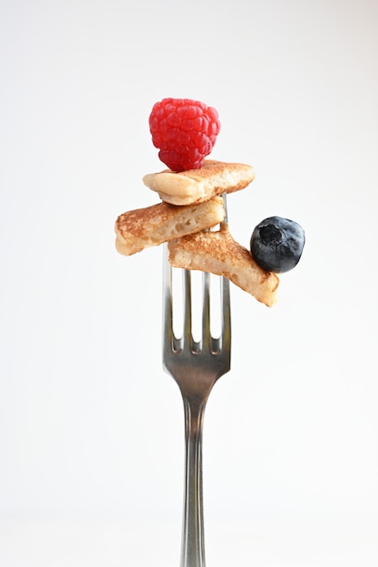 Pancake on a fork with strawberries on white background.