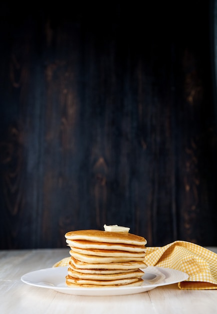 写真 木製の背景にバターのかけらと白い皿の上のパンケーキ