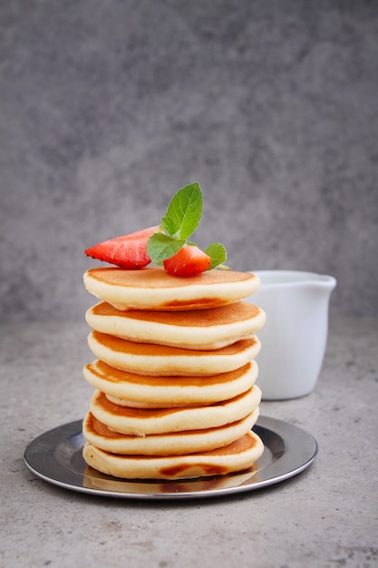 Pancake in un piatto con fragole decorate con menta su un tavolo di cemento