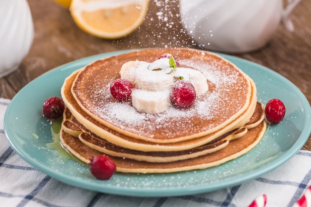 Pancake stack covered with honey, powdered sugar, banana and cranberries.