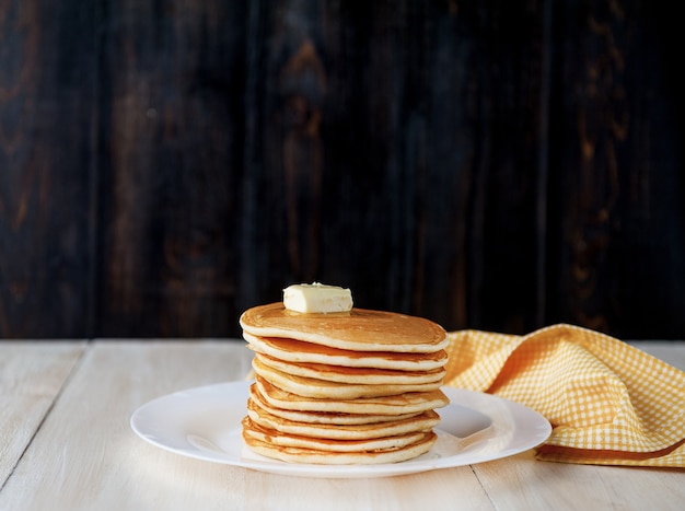 Pancake on a white plate with a piece of butter on a wooden background