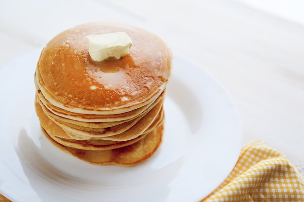 Pancake su un piatto bianco con un pezzo di burro su un fondo di legno