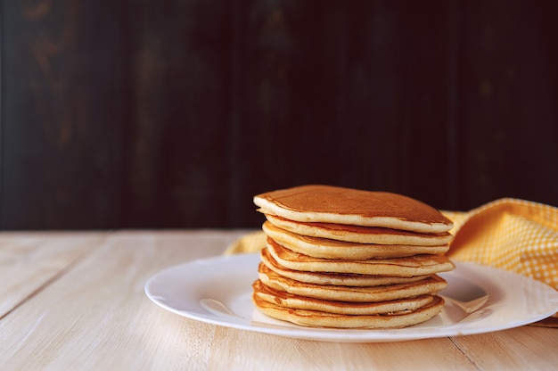 Pancake su un piatto bianco su un fondo di legno