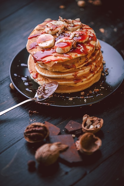 Pancake con cioccolato e pasta di noci, noci e banana su un piatto nero