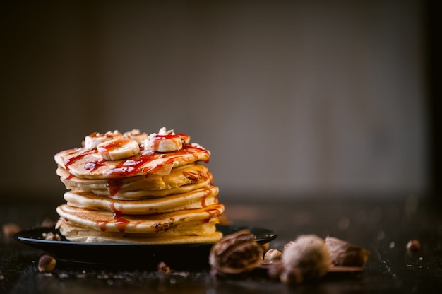 Pancake con cioccolato e pasta di noci, noci e banana su un piatto nero