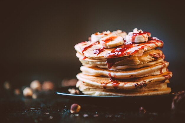 Pancake with chocolate and nut paste, walnuts and banana on a black plate