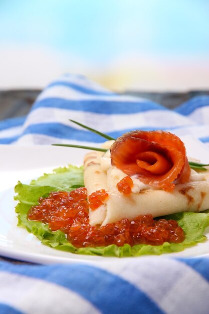 Foto pancake con caviale rosso salmone e cipolla verde maionese su piatto su tovagliolo colorato su tavola di legno su sfondo luminoso