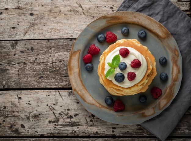 Pancake with vanilla cream, blueberries and raspberries. Top view, copy space. Old rustic 