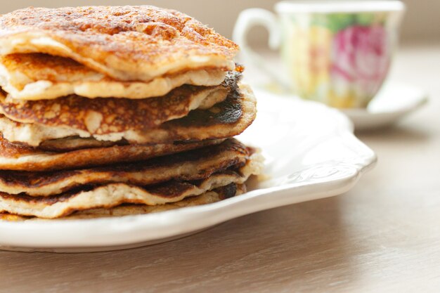 Pancakes almond coconut flour stack on white plate and cup on wooden table background