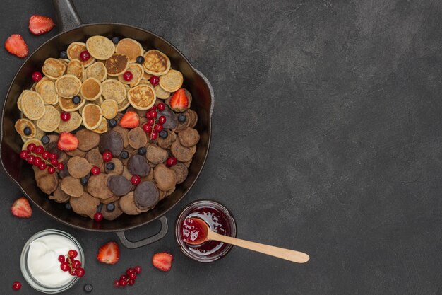 Pancakes and berries in pan Yogurt and jam on table Black background Flat lay Copy space