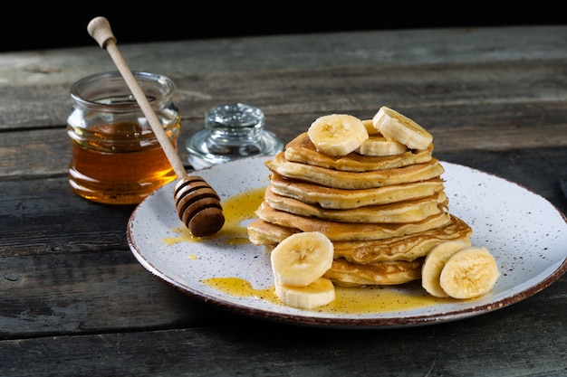 Foto frittelle sul piatto in ceramica servito con banane e miele su legno