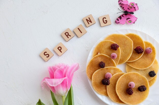 Photo pancakes flowers and spring inscription on a white background