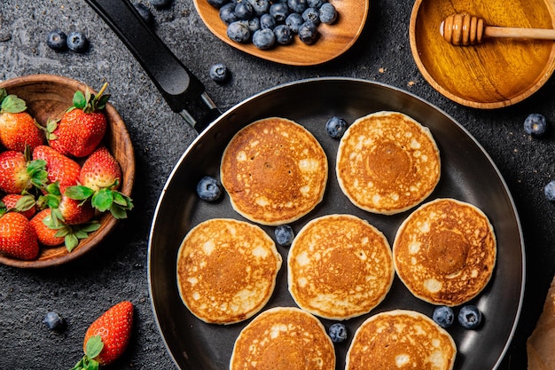 Pancakes in a frying pan with fresh berries and honey