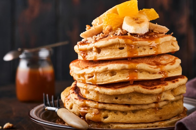 Pancakes. pancake soffice fatto in casa con banana, noci e caramello per colazione su fondo di legno scuro. deliziose frittelle per la tradizionale colazione americana. messa a fuoco selettiva. modello.