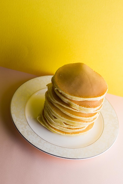 Pancakes on pink yellow background many homemade pancakes on white plate delicious dish for breakfast festive food on colorful background