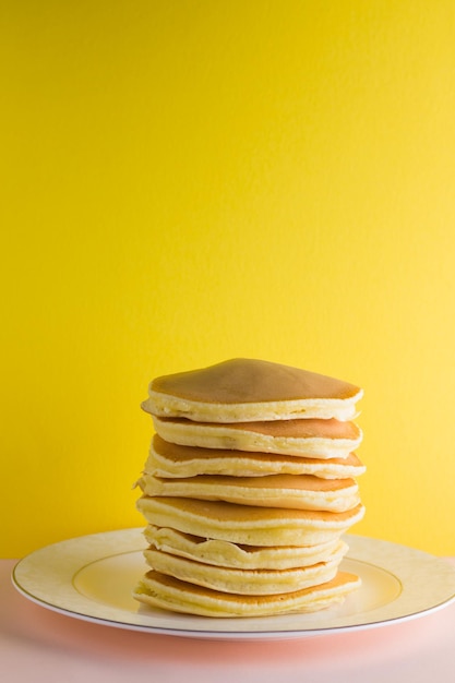 Pancakes on pink yellow background many homemade pancakes on white plate delicious dish for breakfast festive food on colorful background