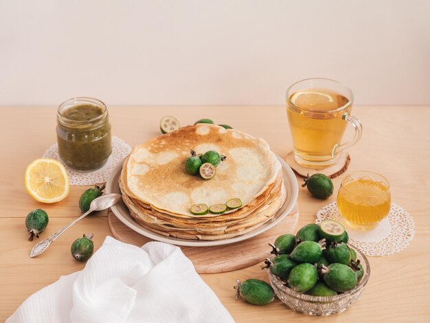 クリスタル花瓶緑茶のフェイジョアフルーツアカシア蜂蜜で飾られたプレート上のパンケーキ