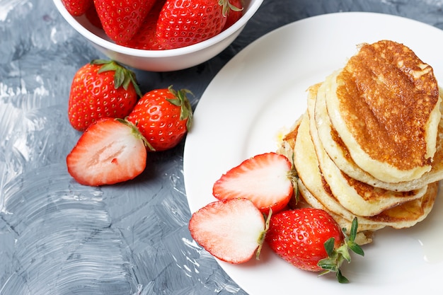 Pancakes on plate and strawberries on a gray background