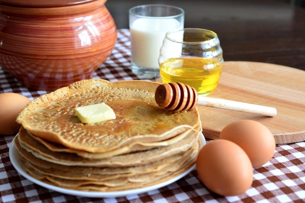 pancakes on plate with honey, milk and ceramic pot and kitchen napkin isolated, close-up