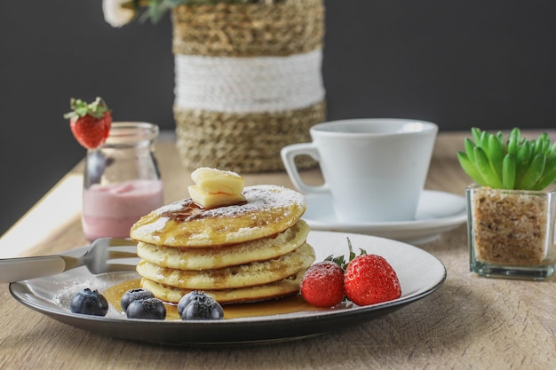 Pancakes served with butter honey and fruirs served on a wooden table